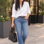Woman wearing a white button-down shirt, blue straight-leg jeans, black loafers and a black tote.